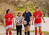 Fire fotballspillere går langs en sti og holder fotballer.